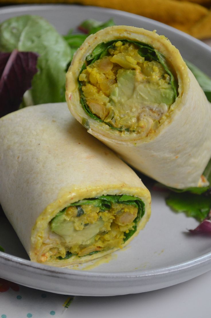 two burritos on a plate with lettuce and other vegetables in the background