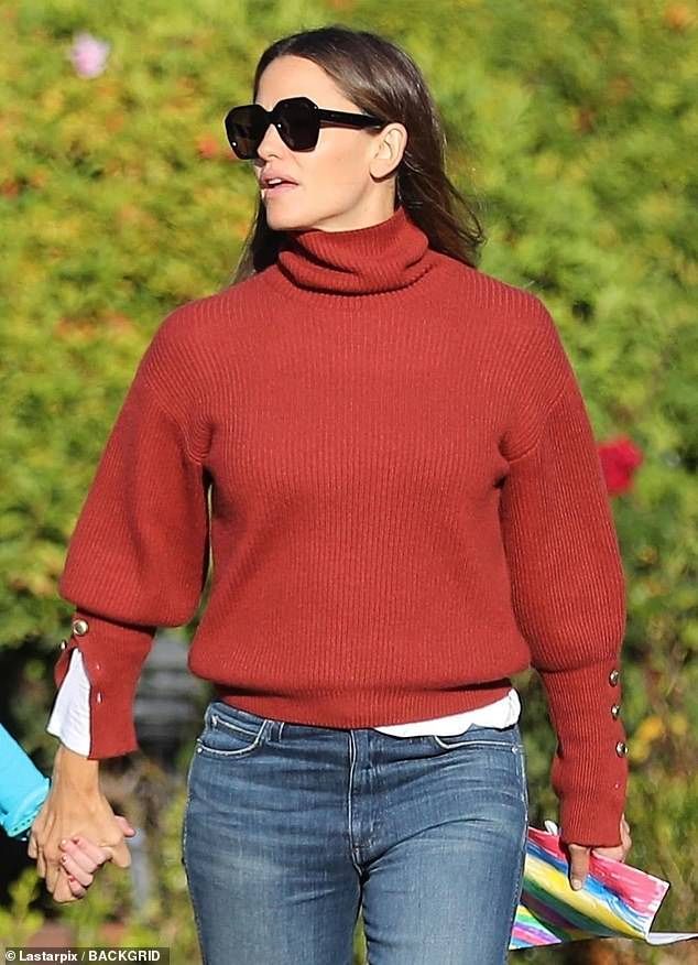 a woman in a red sweater and jeans holding hands