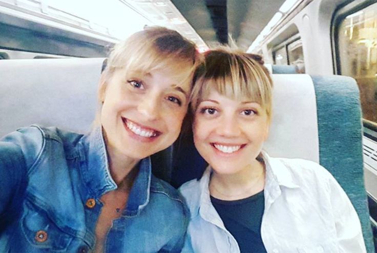 two women are taking a selfie on a train together, one is wearing a denim jacket and the other has blonde hair