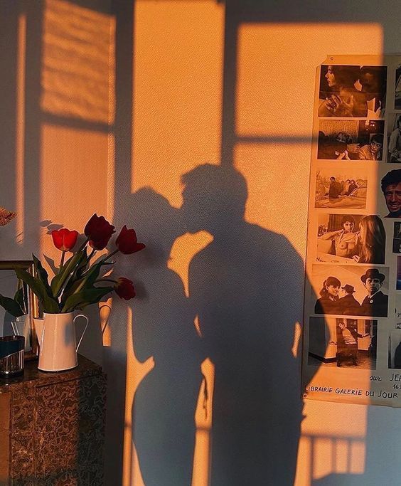 the shadow of a man and woman standing in front of a wall with pictures on it