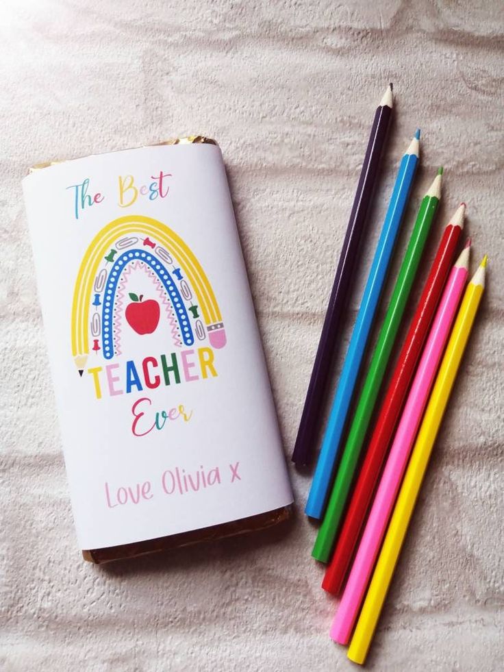 several colored pencils are next to a teacher's book with an apple on it