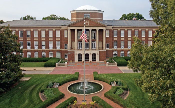 an old brick building with a fountain in the center and flags on it's roof