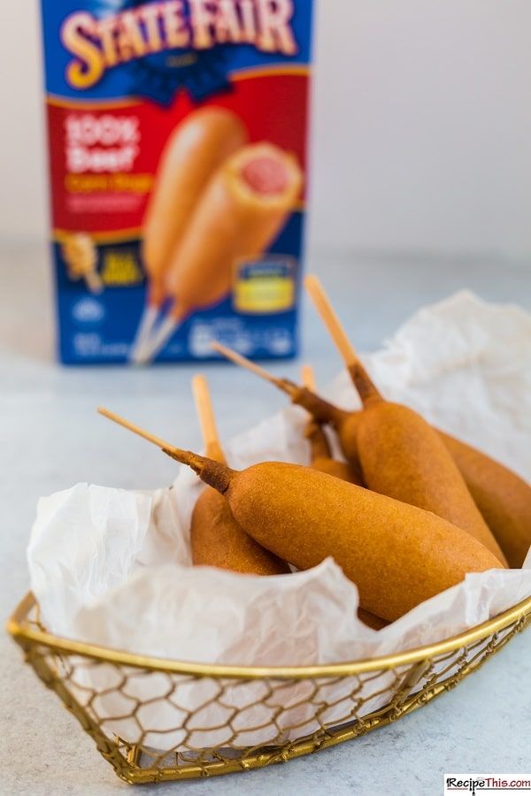 three hot dogs in a basket next to a carton of tater tot