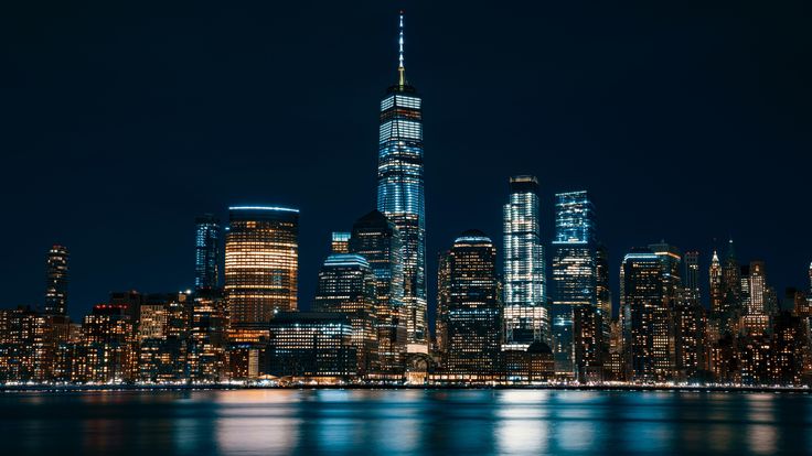 new york city skyline at night with the empire building lit up in blue and white