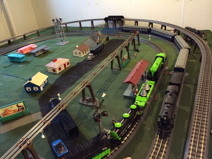 a model train set up in a room with people looking at the trains on tracks