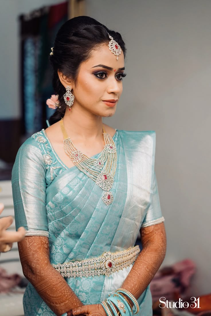 a woman in a blue sari with jewelry on her neck and hands behind her back