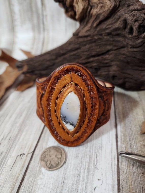 Check out this item in my Etsy shop https://www.etsy.com/listing/1390418259/dendrite-opal-tooled-leather-cuffstone Handmade Western Style Cuff Bracelets, Rustic Hand Tooled Leather Jewelry, Artisan Handcrafted Brown Jewelry, Leather Concho Cuff Bracelet Gift, Artisan Stamped Brown Jewelry, Leather Concho Cuff Bracelet As A Gift, Western Leather Jewelry With Concho, Vintage Hand-tooled Brown Jewelry, Vintage Brown Hand-tooled Jewelry