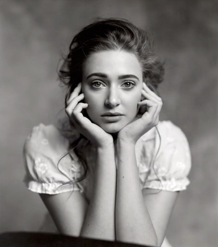 an old black and white photo of a woman with her hands on her face, sitting at a table