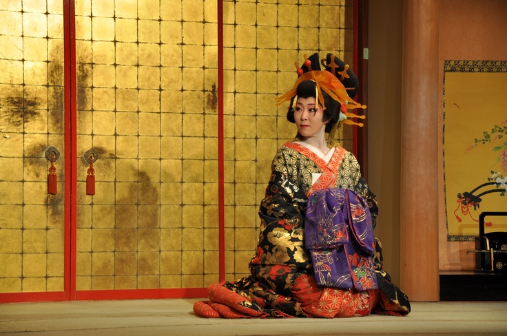 a geisha sitting on the ground in front of a wall