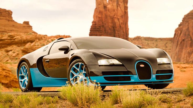 a bugatti car parked in the desert near some rocks and grass with mountains in the background