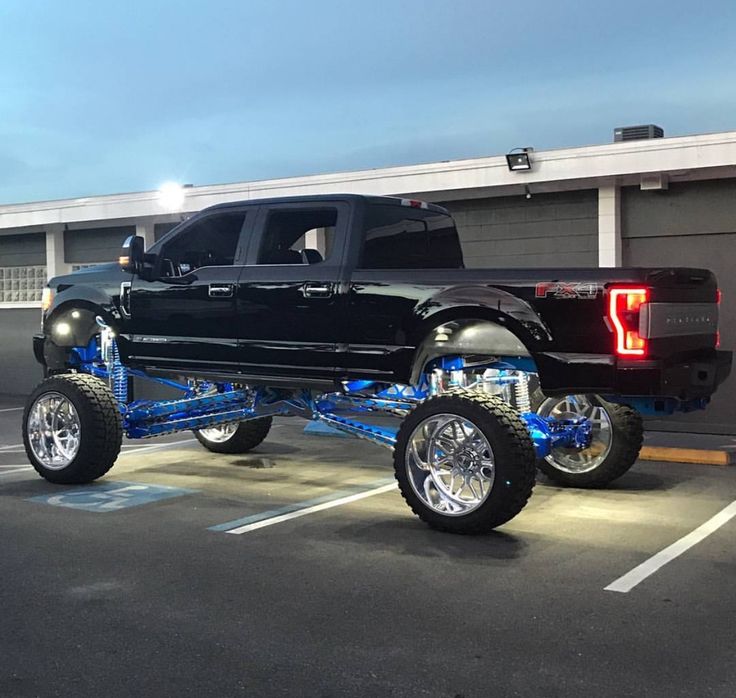 a large black truck parked in a parking lot next to a building with lights on