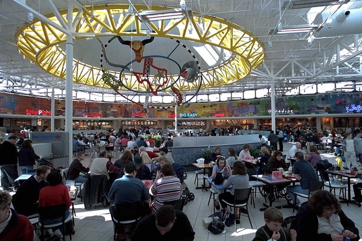 a large group of people sitting at tables in a building with lots of windows on the ceiling