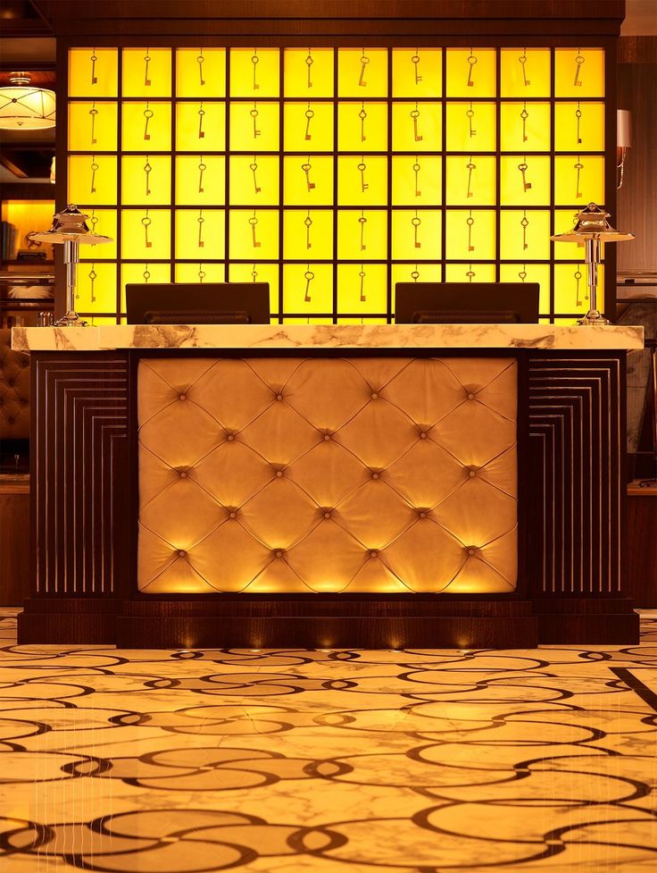 the front desk of a hotel lobby with yellow lights behind it and an area rug on the floor