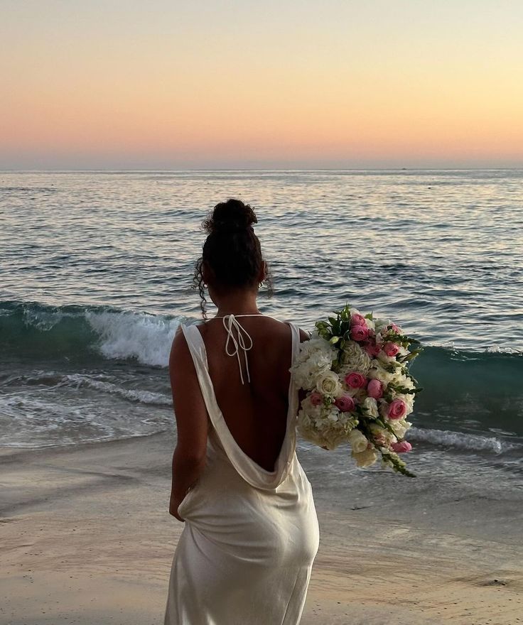 a woman in a white dress is standing on the beach with her back to the camera