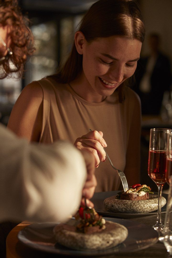 a woman sitting at a table in front of a plate with food on it and a glass of wine