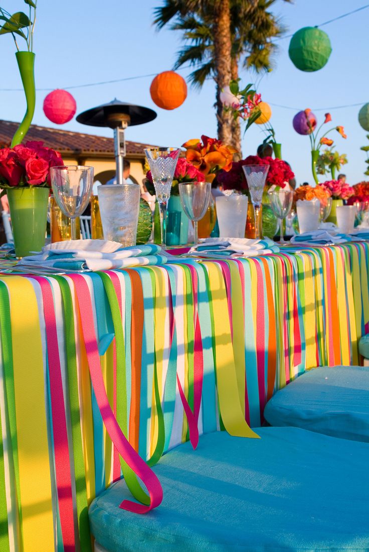 colorful table cloths and vases are set up for an outdoor party with palm trees in the background