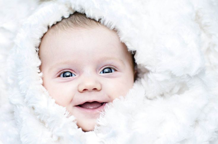 a baby is smiling while wrapped in white fluffy blankets and looking up at the camera