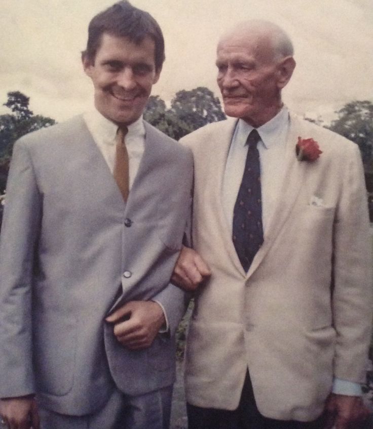 two men in suits and ties standing next to each other with trees in the background