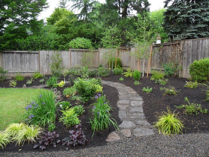 a garden with lots of different plants and flowers in it's center, next to a wooden fence