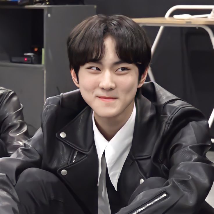 a young man wearing a black leather jacket and white shirt sitting in front of a table