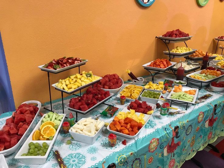 a table topped with lots of trays of fruit on top of a blue table cloth