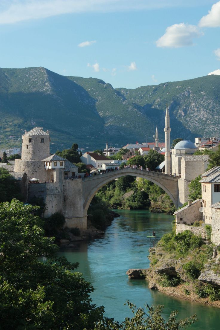 an old bridge over a river with buildings on both sides and mountains in the background