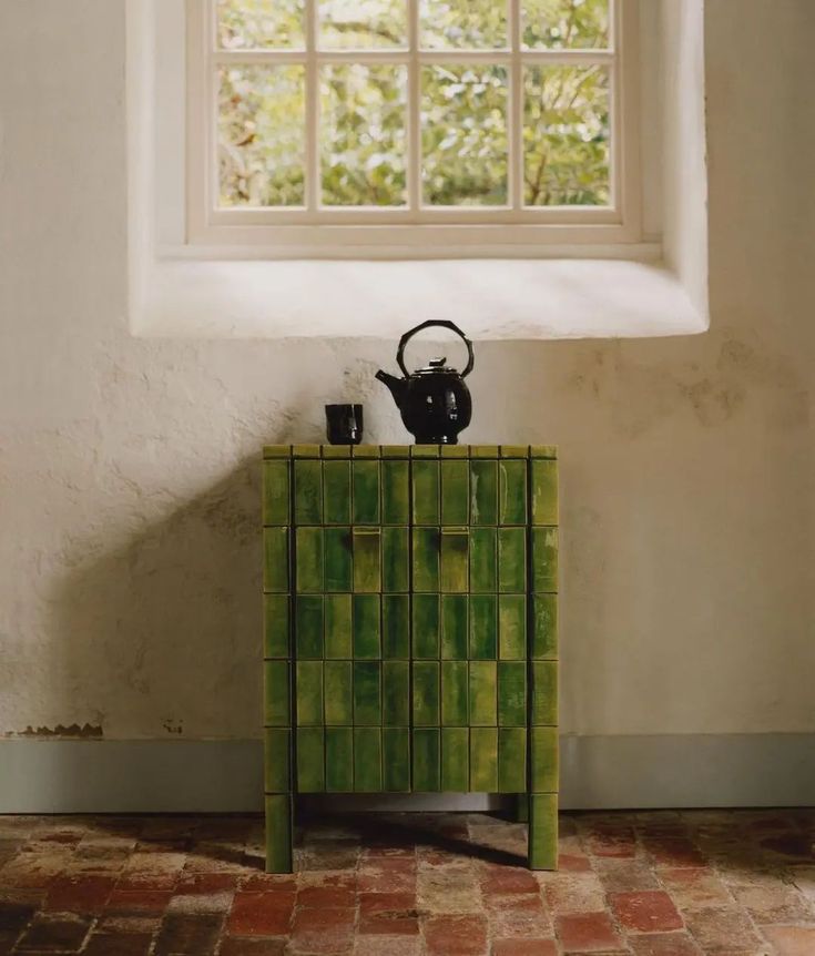 a green cabinet sitting in front of a window with a tea pot on top of it