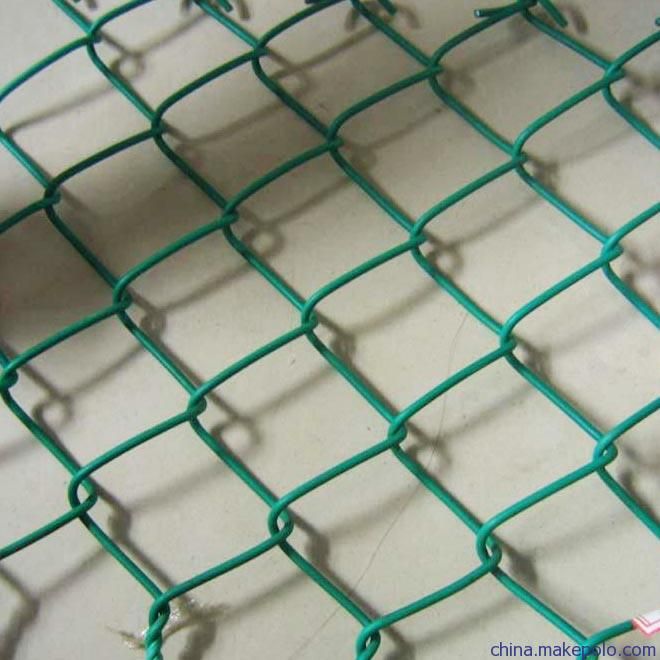 green wire mesh fence with holes on the top and bottom, in front of a white wall