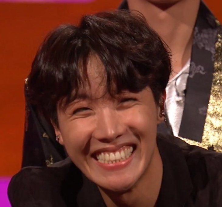 a smiling young man sitting in front of a tv screen with other people behind him