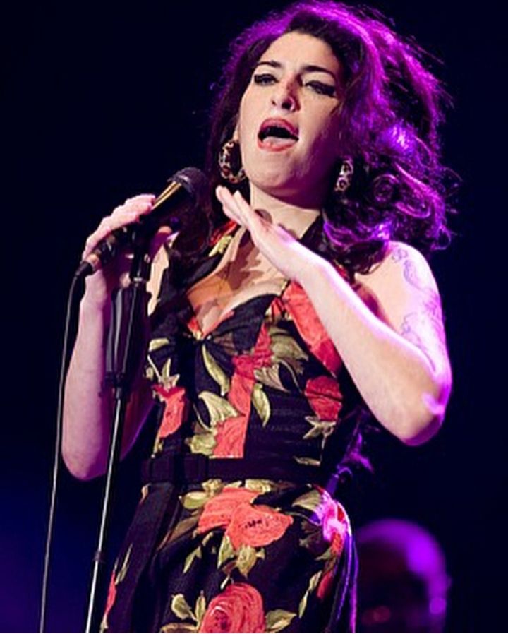 a woman singing into a microphone while wearing a floral dress and holding her hands out