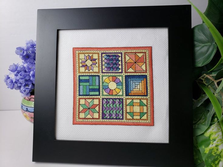 a cross - stitch pattern in a black frame on a table next to purple flowers