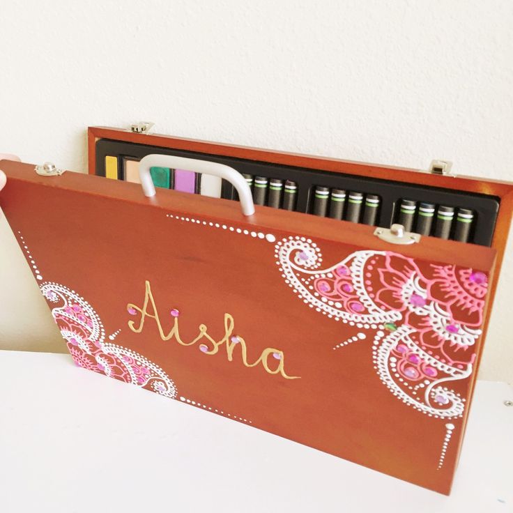 a wooden box with pens and markers in it sitting on a table next to a white wall