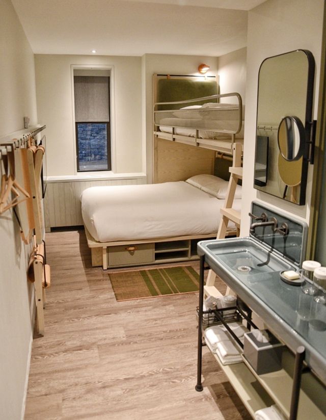 a bedroom with bunk beds, sink and mirror in it's corner next to a bathroom