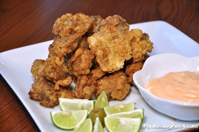 some fried food on a white plate with lime wedges and sauce in a bowl