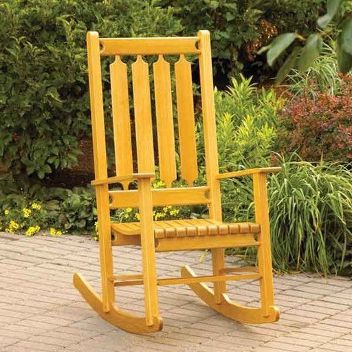 a yellow rocking chair sitting on top of a brick floor next to bushes and trees