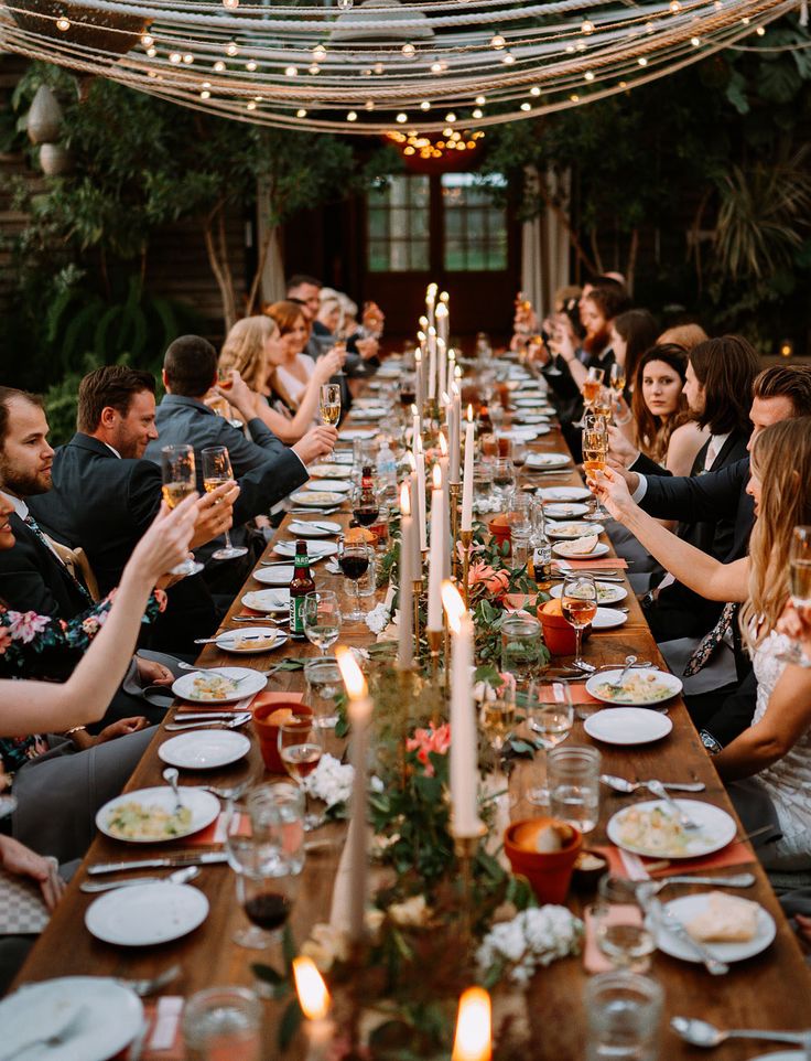 a group of people sitting at a long table with plates and wine glasses on it