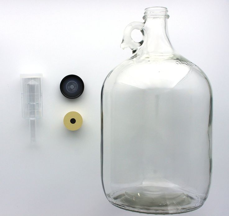 an empty glass bottle next to a small plastic object on a white surface with other items around it