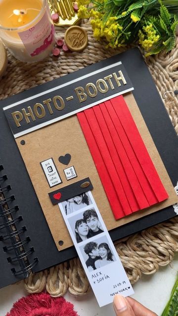 an open photo booth with red curtains and flowers on the table next to it is a person holding a card