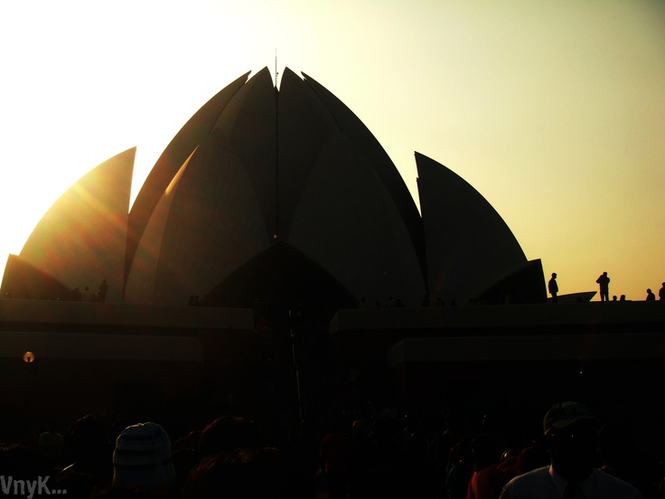 the sun is setting behind a large building with many people standing in front of it