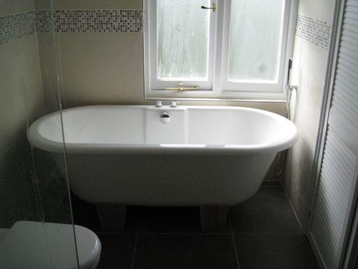 a white bath tub sitting next to a toilet in a bathroom under a large window