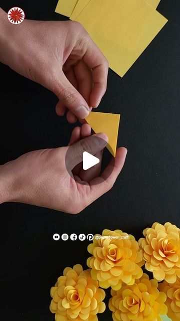 two hands are holding yellow flowers and making paper decorations on a black surface with white circles around them