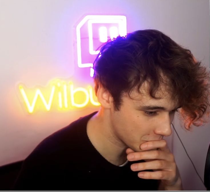 a man with his hand on his face in front of a neon sign that reads wild