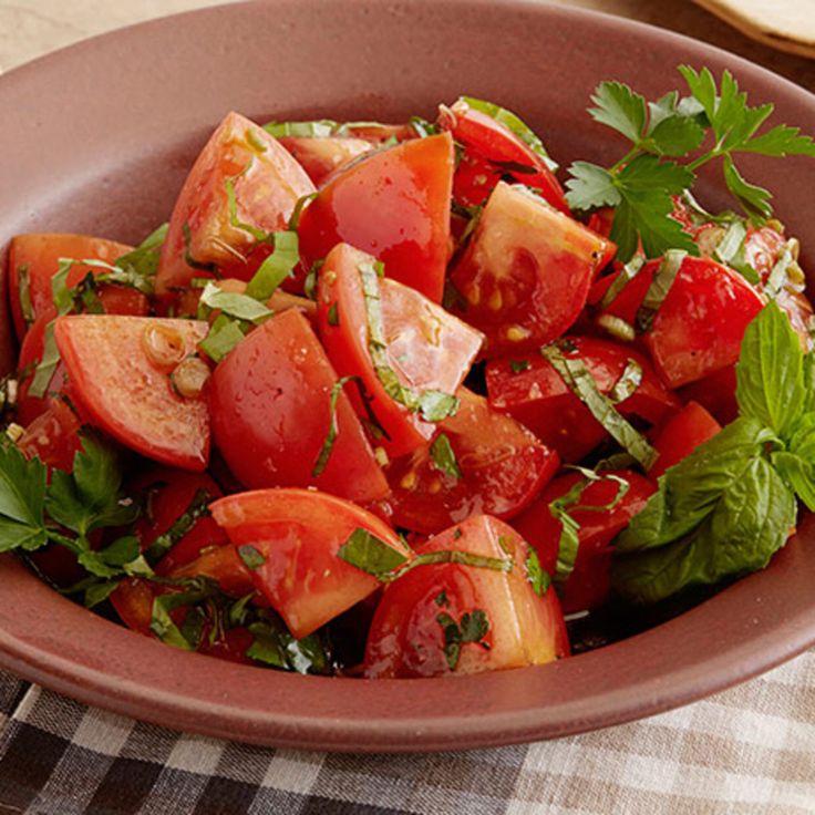 a brown bowl filled with sliced tomatoes and green garnish on top of a checkered table cloth