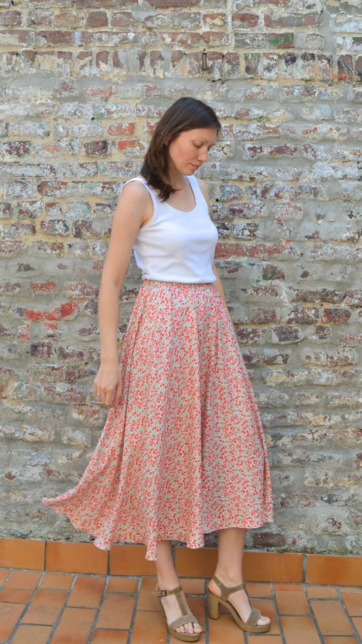 a woman standing in front of a brick wall wearing a white top and floral print skirt