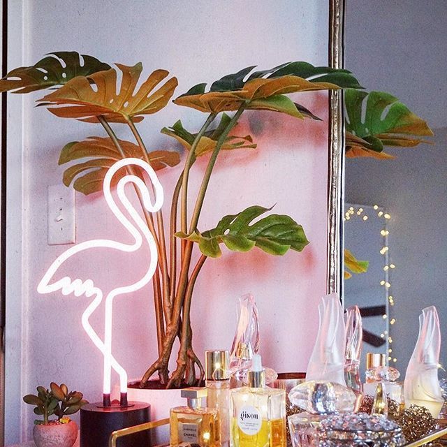 a pink flamingo neon sign sitting on top of a table next to a potted plant