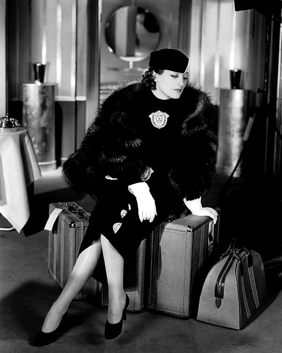 a black and white photo of a woman sitting on luggage