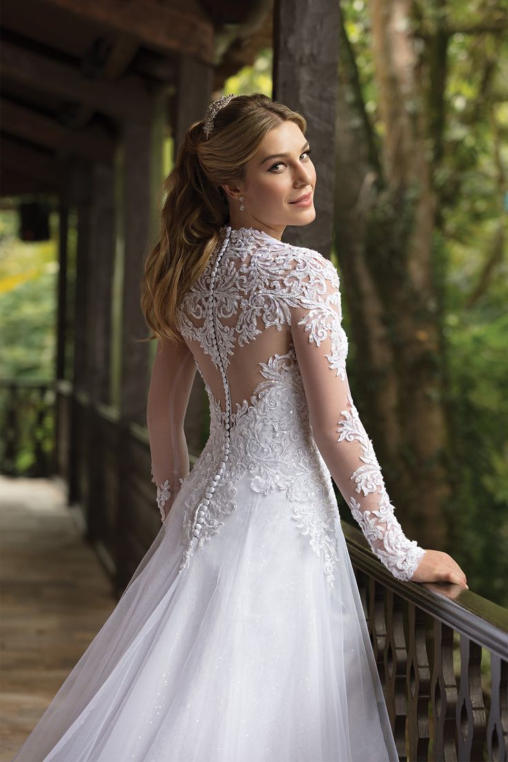 a woman in a white wedding dress standing on a bridge with her back to the camera