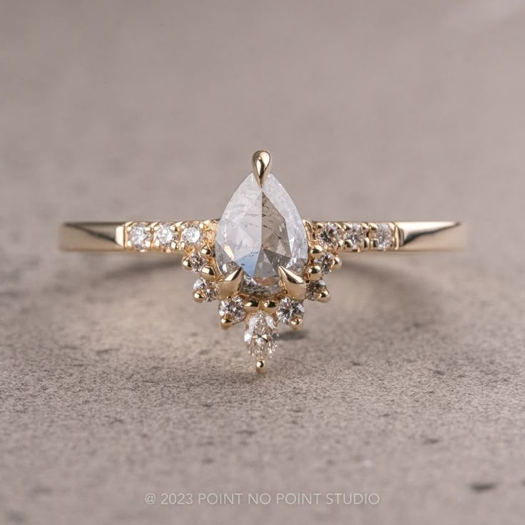 a gold ring with a pear shaped diamond surrounded by smaller round brilliant cut white diamonds