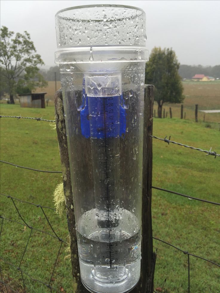 a plastic water bottle sitting on top of a wooden post in front of a fence