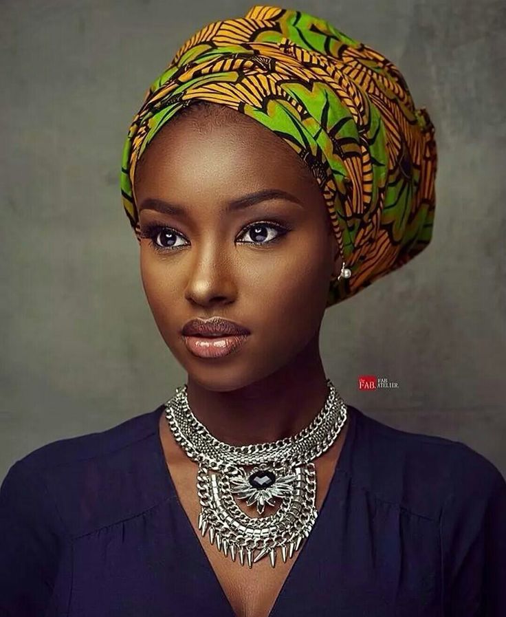 an african woman wearing a green and yellow head wrap with necklaces on her neck